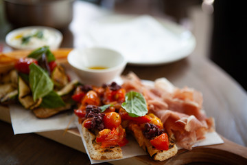 Delicious and colorful Bruschetta topped with grilled cherry tomatoes together with Prosciutto di Parma or Parma ham and grilled vegetable on a wooden board. Natural light. Focus at Bruschetta.