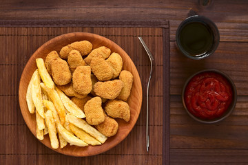 Frische knusprige frittierte und panierte Chicken- oder Hähnchen-Nuggets mit hausgemachten Pommes Frites, fotografiert mit natürlichem Licht