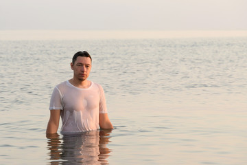 Young man standing on his chest in the sea water and calmly looking