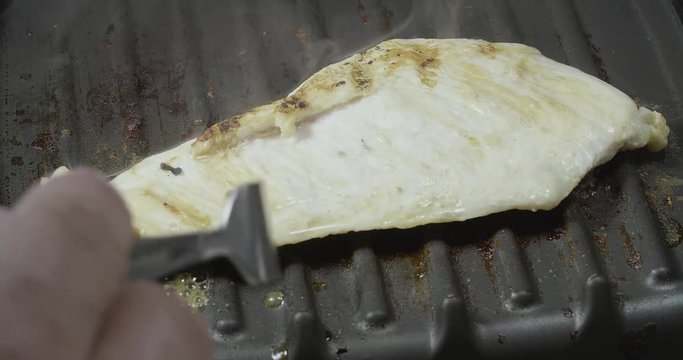 close up of a chicken being grilled while letting out smoke in a grill surrounded by grease looking delicious and then being flipped to another side with a metal fork