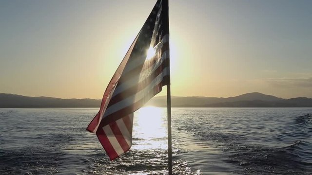 USA Flag Waving in the Wind on the Ocean at Sunset. Backlit Silhouette Footage.
