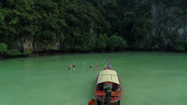 Flying around taxi boat with people at hong island lagoon in thailand. Beautiful colorfull excotic paradise nature with turquoise ocean water while traveling - aerial drone shot