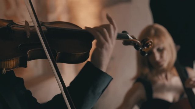 Close up shot of a male violinist playing his violin in a string quartet with a female cellist in the background