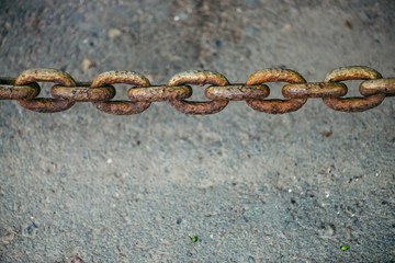 Old oxidized rusty chain hanging over asphalt close up with copy space. Conceptual background with thick links of strong chain. Artwork.