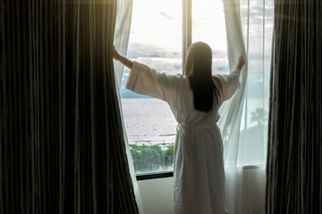 Back side of Asian woman in bathrope suit when waking up from the bed in luxury hotel in morning, Life style and holiday concept