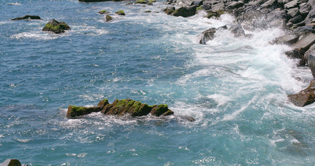 Breaking waves beating and rolling stones at sea coast