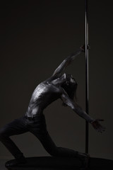 Sexy macho with metal skin. Athletic man make acrobatic elements on pylon. Pole dance sport. Muscular man with silver body art dancing on pylon. Moving to his goal. dancer workout on pole. Freedom