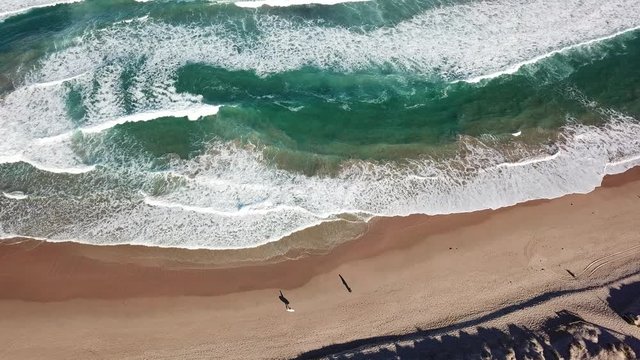 Seascape with waves and shadows of walking people. Top view aerial photo from flying drone of nature landscape turquoise water with Wanda beach in winter day in Cronulla. Travel vacation concept.