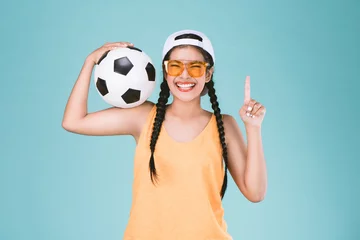 Gordijnen Fan sport woman smiling and happy, holding a soccer ball,celebrating point one finger up winner sign © Ratthaphon Bunmi
