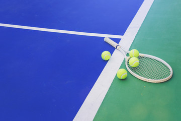 Tennis racket and tennis balls laying on hard court in blue and green with white line.