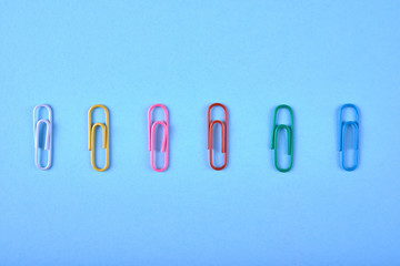 Colorful paper clips isolated on pink background, close up, copy space. Top view, flat lay. Back to school, college, education concept. White, orange, pink, red, blue paperclips