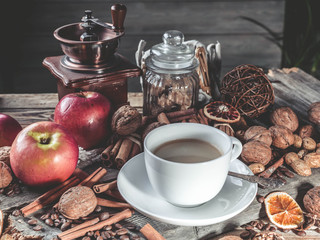 White espresso cup on vintage background. Cinnamon sticks, nuts, apples, coffee beans. Vintage composition. Light toning