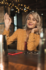 Hey there. Tipsy young woman sitting at the bar counter and waving at someone, having noticed them