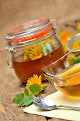 Close-up of dandelion honey, spoon, dandelion head around and full jar in background - vertical photo