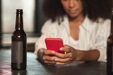 Waiting for updates. The focus being on the phone in the hands of a pretty young woman sitting at the bar counter, drinking beer and checking her device