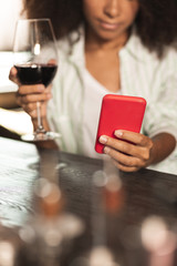 Relaxing break. Charming young woman sitting at the bar counter and drinking her wine while checking the phone for updates
