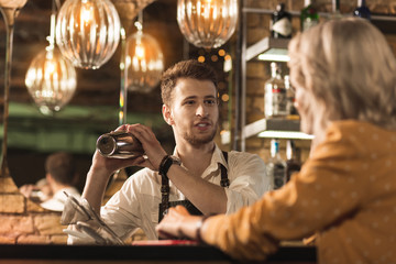 Nice conversation. Handsome male barman chatting with his female customer while mixing a cocktail in the shaker