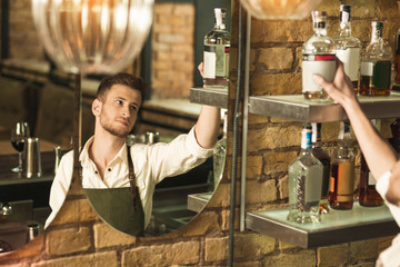 Diligent worker. Handsome young barman taking a bottle of alcohol from the shelf while mixing a cocktail