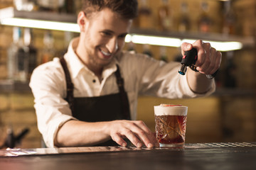 Special equipment. Joyful professional barman standing behind the bar counter and using a culinary torch to burn the sugar on his cocktail