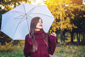 Happy young woman walking in a Sunny Park with a white umbrella in the rain. Concept of seasons and...