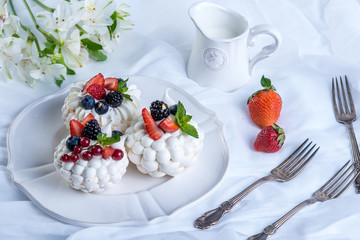 Delicate white meringues with fresh berries on the plate. Dessert Pavlova. A festive wedding cake.