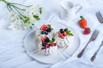 Delicate white meringues with fresh berries on the plate. Dessert Pavlova. Festive wedding cake.