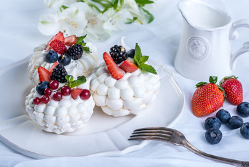 Delicate white meringues with fresh berries on the plate. Dessert Pavlova. Festive wedding cake.