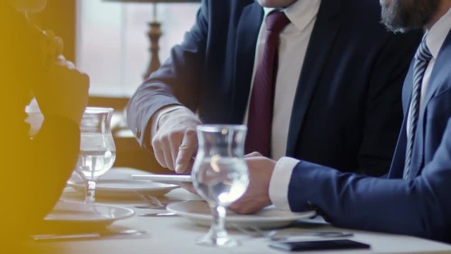 Tilt up shot of three business people sitting at table in cafe or restaurant during business lunch and using tablet computer when discussing agreement