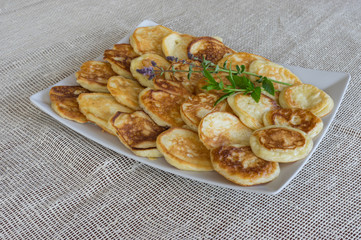 Plate full of pancakes with branches of mint standing on a table covered with textile table-cloth