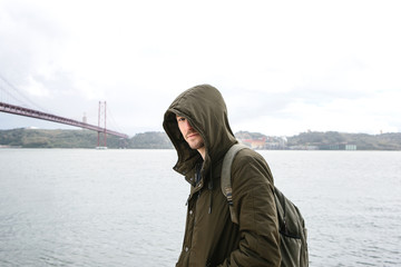 A young traveler or a tourist with a backpack on the waterfront in Lisbon in Portugal next to the 25th of April Bridge