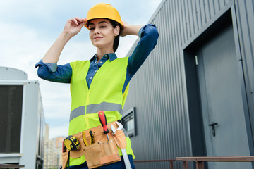 confident female architect with tool belt in safety vest and helmet