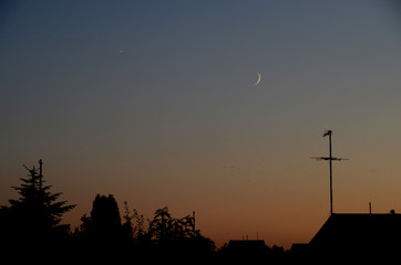 Conjunction between the crescent Moon and Venus seen in the evening in urban surroundings.