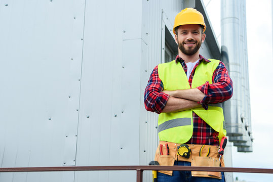 male professional engineer with tool belt posing with crossed arms