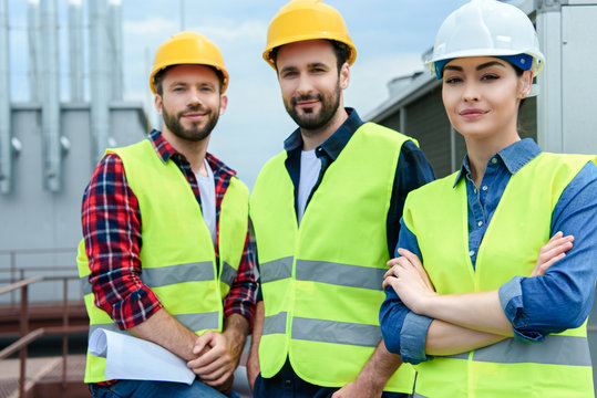 professional engineers in safety vests and hardhats posing with crossed arms