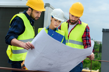 professional engineers in hardhats working with blueprint and clipboard on construction