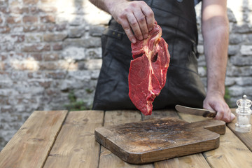 A man is cutting meat for dinner. Beef in the hands of a man. Red meat and an old wooden board. Copy space.