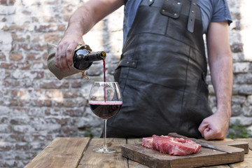 The man cuts the meat for dinner and pours a glass of red wine from the bottle. A party with food and alcohol. Copy space.