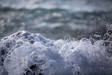 Foamy white breaking waves splash over the rocks on the shoreline