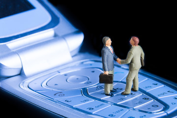 Business deal or agreement and success concept. Two miniature businessmen shaking hands while...