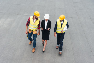 overhead view of female architect and male workers in helmets with clipboard and blueprints