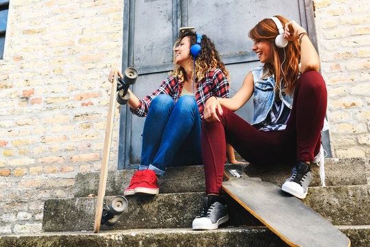 Skate girls sitting in the street hanging out listening music with earphones and smartphone