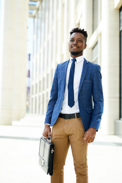 Pensive ambitious young black entrepreneur in formalwear holding briefcase  and looking around while standing at office building Stock Photo | Adobe  Stock