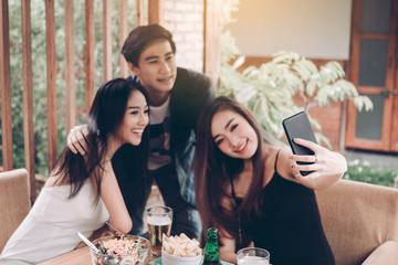 Asian friends smiling and taking selfie in restaurant.