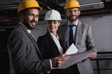 architects in suits and helmets working with blueprint and digital tablet on construction together
