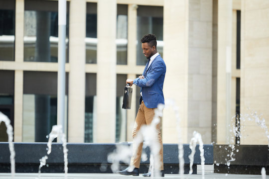 Serious busy handsome black man in formalwear being late for meeting and checking the time while walking over city street - Powered by Adobe
