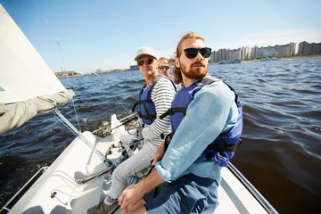 Photo sur Plexiglas Naviguer Des hommes calmes sérieux dans des gilets de sauvetage et des lunettes de soleil assis en rangée sur un yacht et regardant autour pendant une excursion de voile sur la rivière