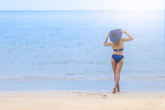 A woman in bikini stand alone on the beach happily.