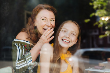 Laughing with daughter. Red-haired beaming woman laughing out loud while standing with her daughter