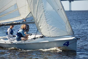 Fototapete Segeln Erfahrene, gutaussehende Männer, die an Segelwettbewerben teilnehmen: junger Hipster-Mann, der mit einem Seil ein Segelboot handhabt, um das Großsegel auf dem Fluss zu lenken