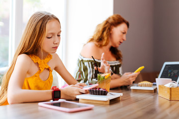 Obraz na płótnie Canvas Modern watch. Blonde-haired schoolgirl wearing modern red smart watch sitting in restaurant near mother